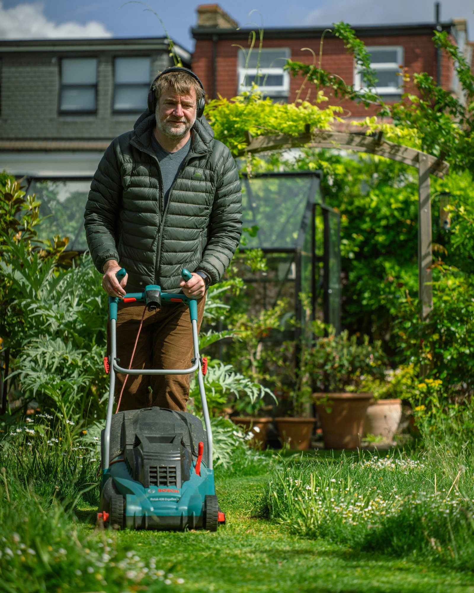 Caucasian man mowing lawn amidst lush greenery in a sunny garden.